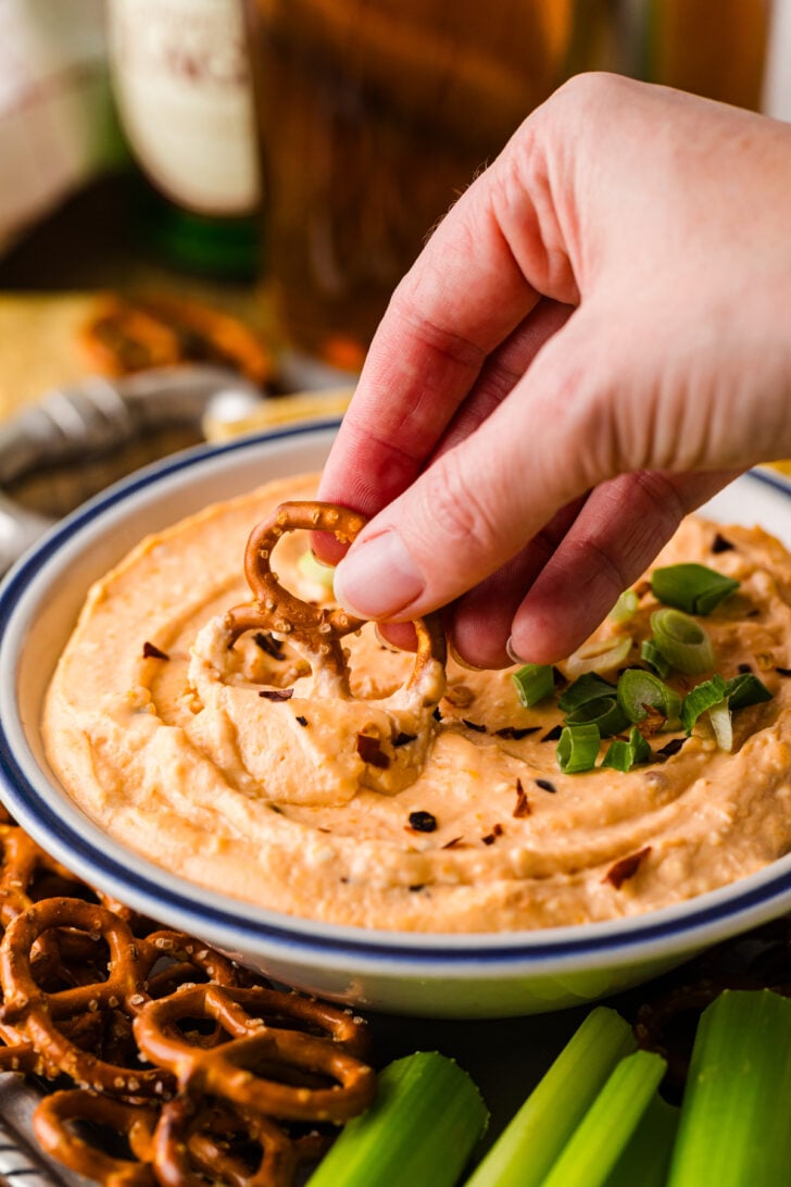 Crock Pot beer cheese dip finished and creamy in a serving bowl, topped with green onion and surrounded by pretzels, chips, and veggies for dipping.
