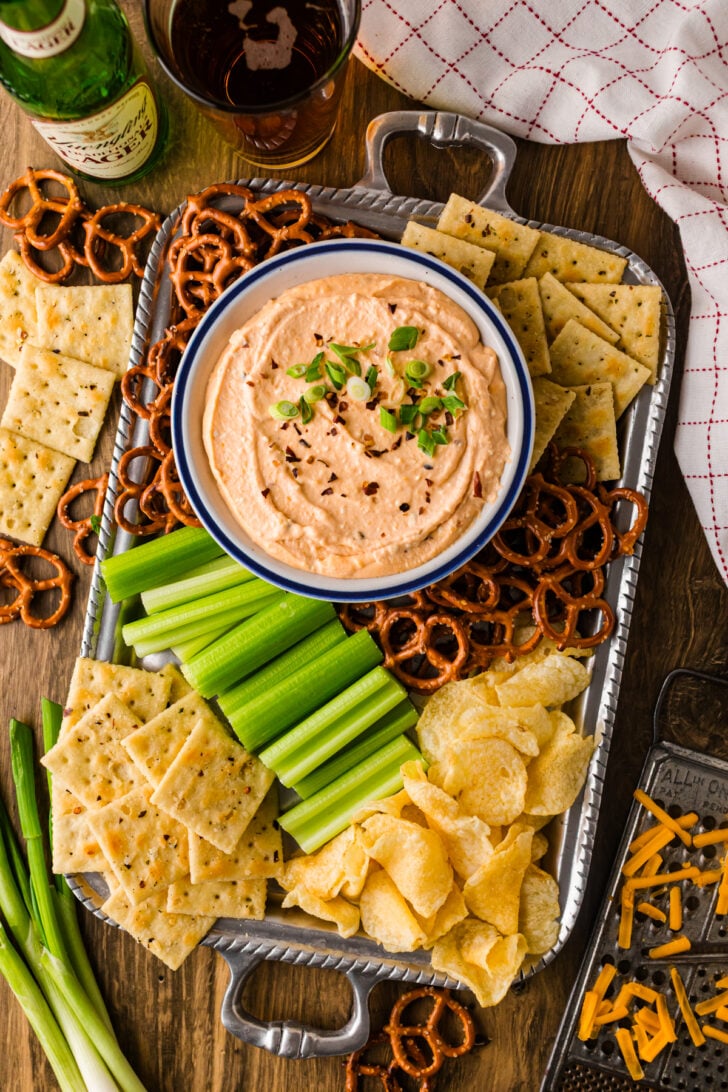 Bowl of Crock Pot beer cheese dip with a full spread of dippers—pretzels, crackers, and fresh veggies like broccoli and carrots.
