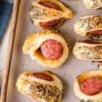 Big Pigs In A Blanket (Puff Pastry + Smoked Sausage) with poppy seeds on parchment paper on a baking sheet