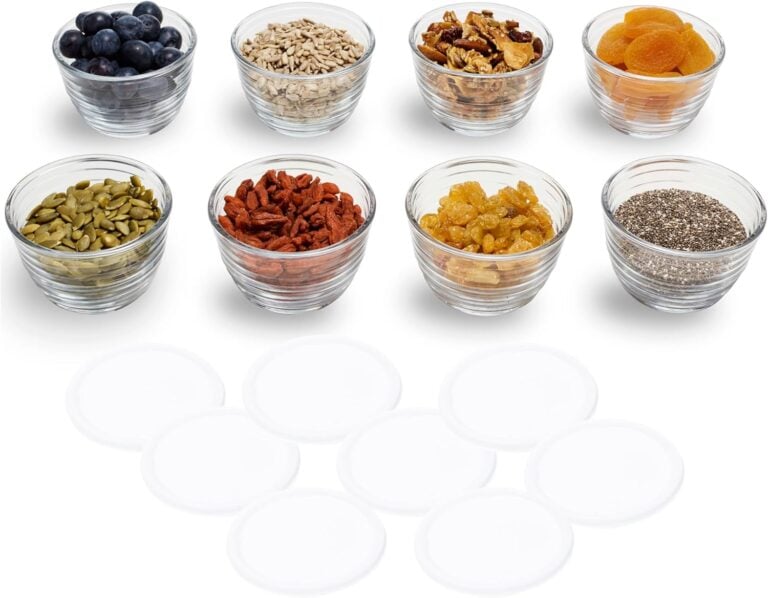 Eight glass bowls containing blueberries, sunflower seeds, walnuts, dried apricots, pumpkin seeds, goji berries, raisins, and chia seeds for
