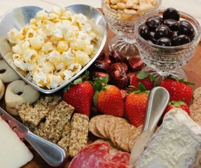 Heart-shaped bowl of popcorn, fresh strawberries, cheese, crackers, olives, nuts, and cured meats arranged for Easy Valentine's Day Dinner f