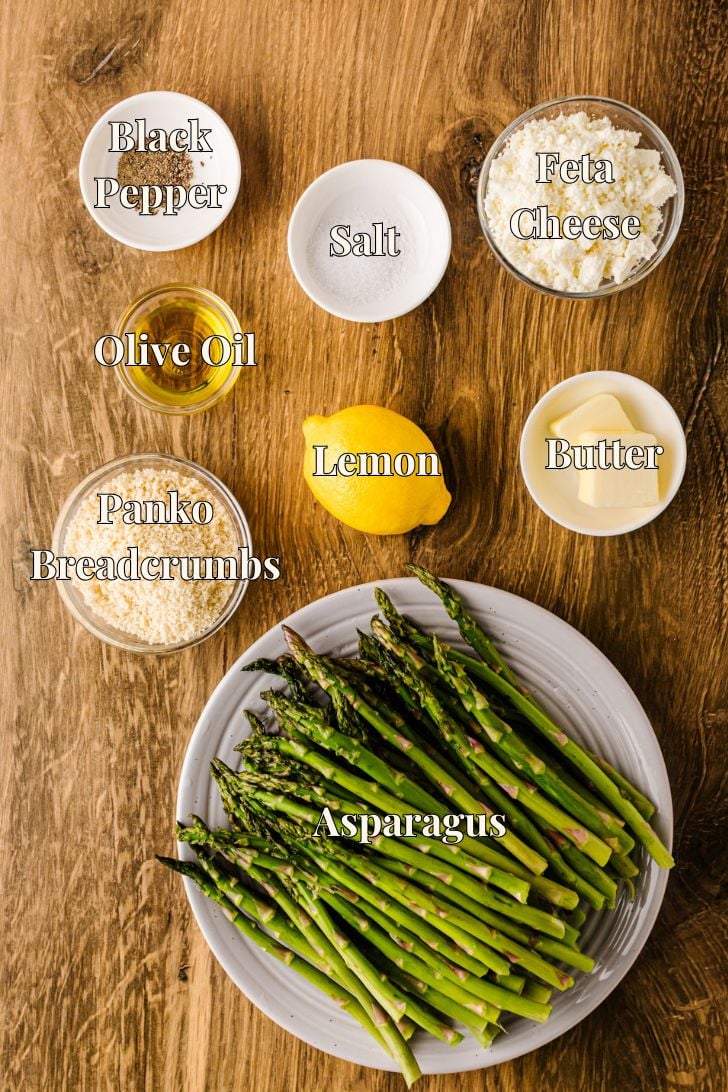 Fresh asparagus spears, panko breadcrumbs, lemon, feta, and butter arranged on a board for roasted asparagus recipe.