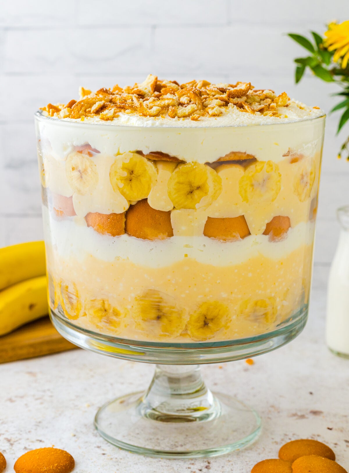 Layered banana trifle 9 e1774833237796 in glass pedestal bowl with vanilla wafers, sliced bananas, creamy custard, and crushed cookie toppin