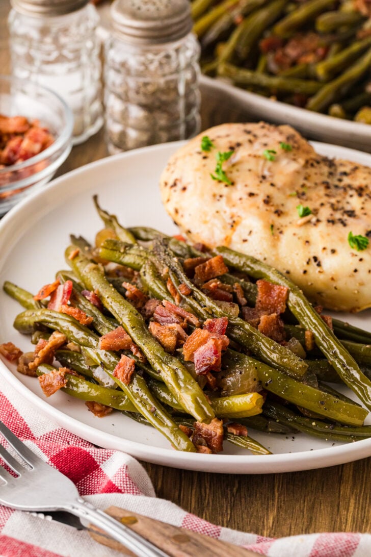 Plate of baked chicken served with a generous helping of maple bacon green beans on the side.