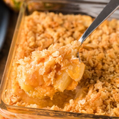 Spoon lifting golden pineapple casserole with crushed cracker topping from glass baking dish