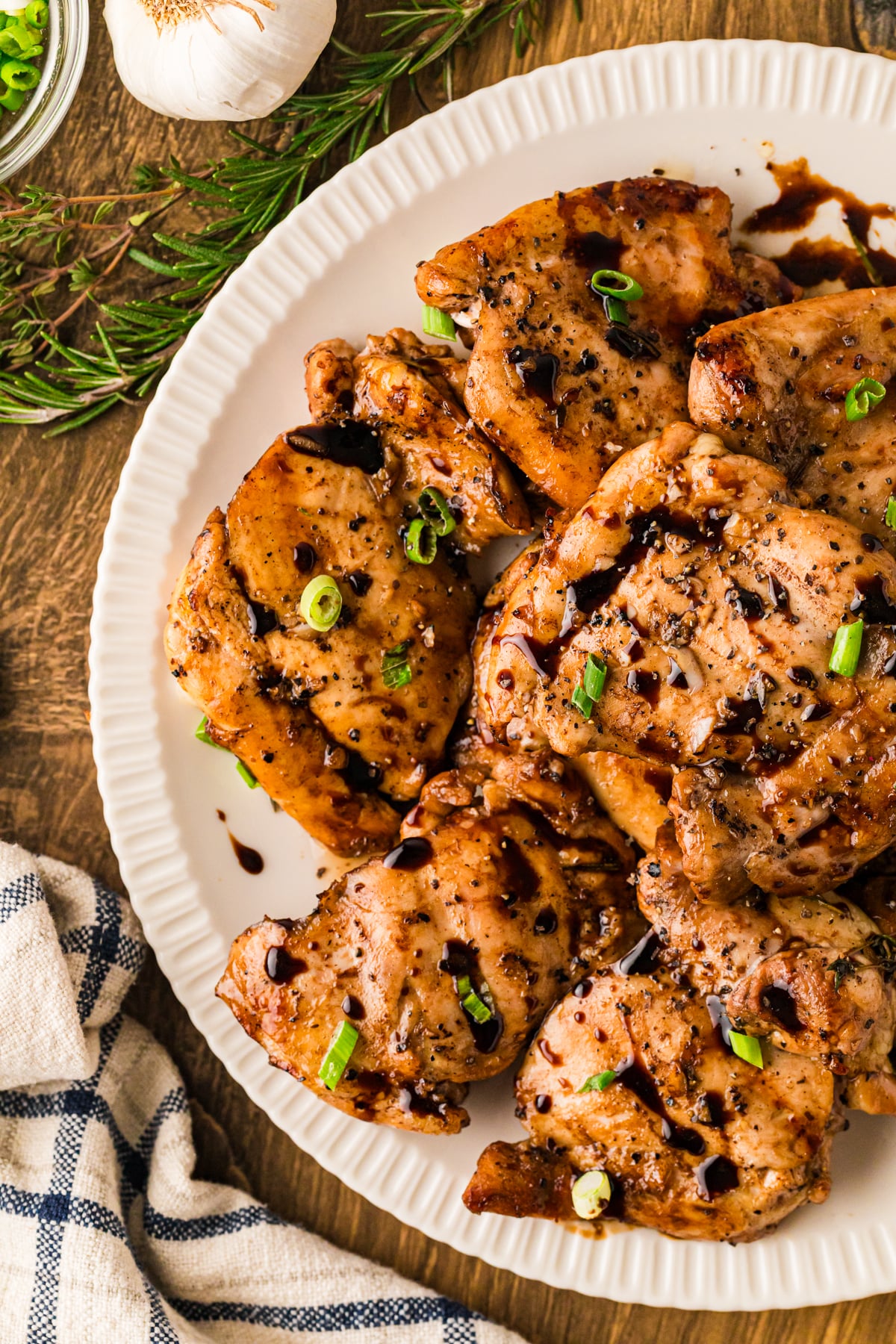Balsamic chicken thighs 10 plated on white dish, topped with green onions and cracked pepper, overhead view on wooden table