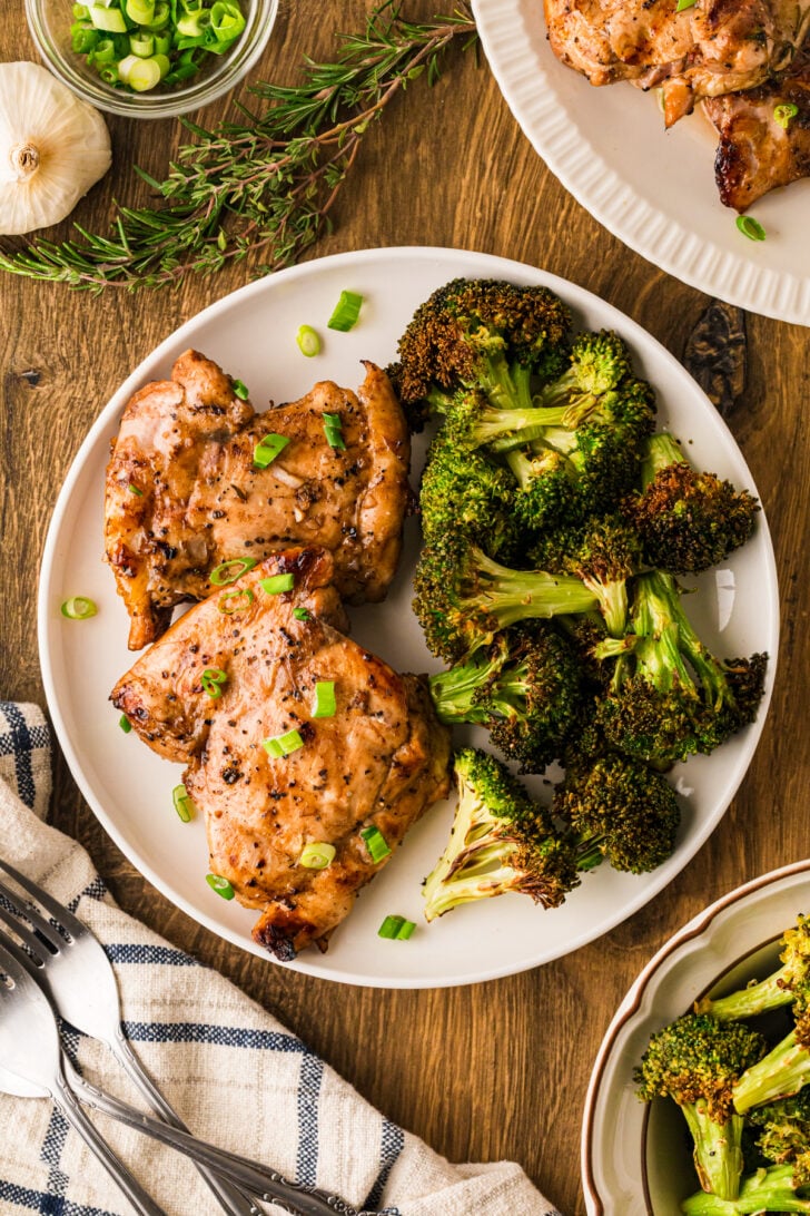 Balsamic glaze chicken thighs on a white plate with roasted broccoli, drizzled with glossy balsamic and green onions.