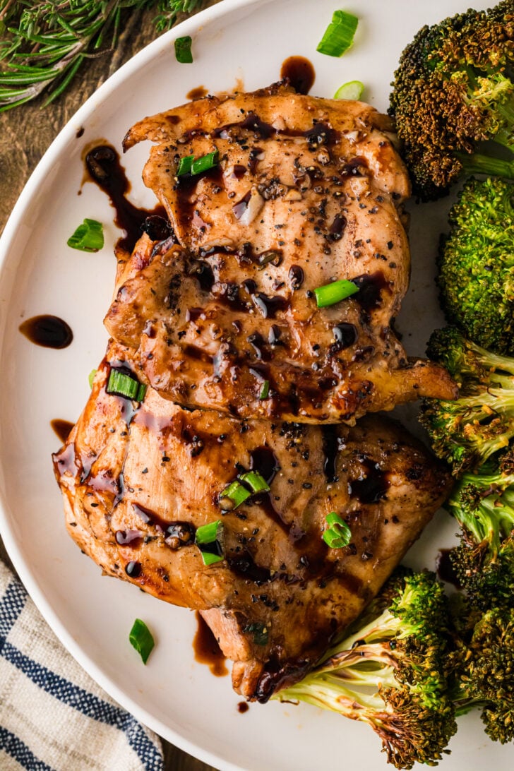 Balsamic chicken thighs glazed with green onions on white plate with roasted broccoli, overhead view
