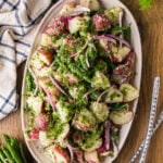 Overhead shot of green bean and potato salad on an oval platter with serving spoons.