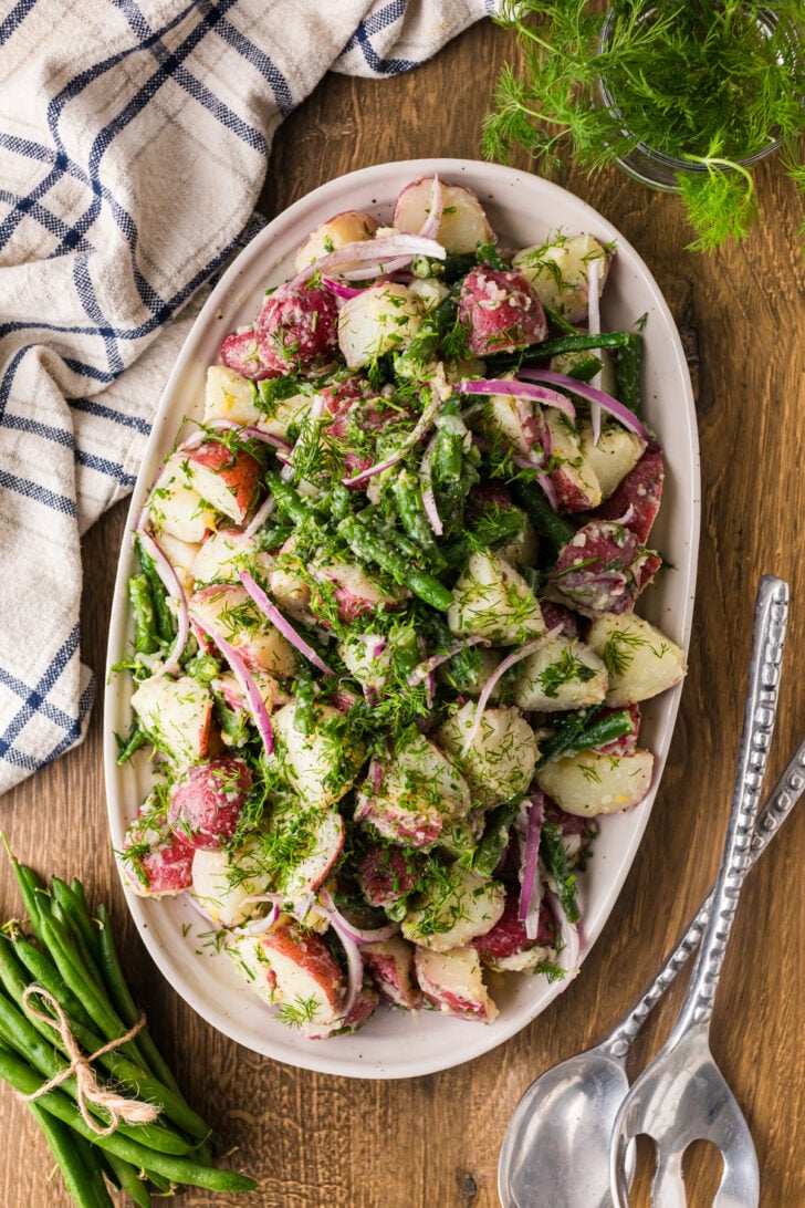 Overhead shot of green bean and potato salad on an oval platter with serving spoons.