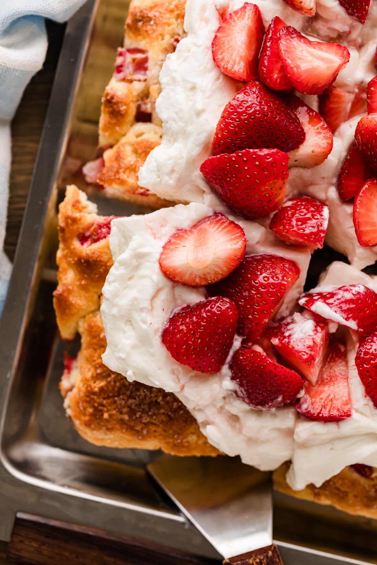 Strawberry Shortcake Sheet Cake in a metal baking pan topped with whipped cream and fresh sliced strawberries, sliced and ready to serve