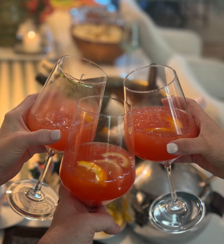 Toasting with three glasses of a citrus cocktail at a brunch gathering.