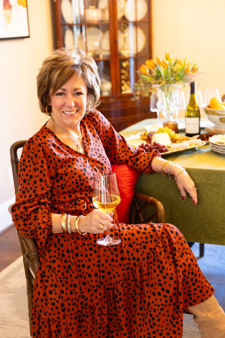 Woman seated at a set dining table with wine and a cheese and fruit spread.