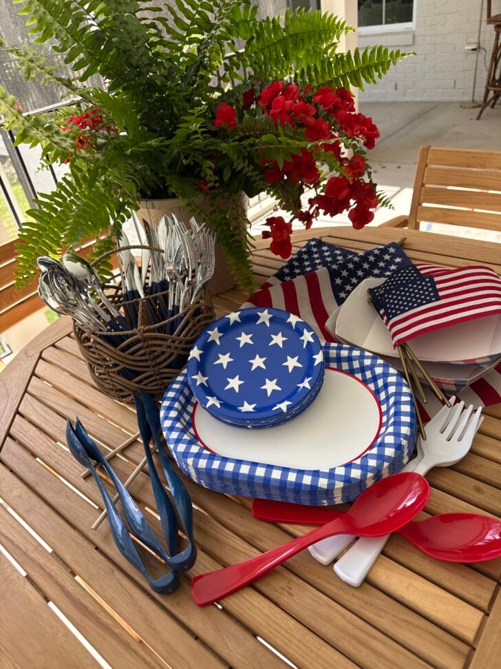 Patriotic table setting with star plates, American flags, and red utensils on an outdoor table.
