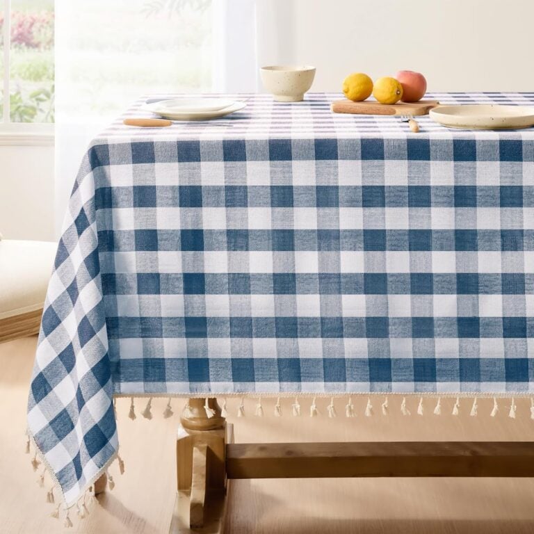 Blue and white gingham tablecloth with fringe on a table set with fruit and dishes.