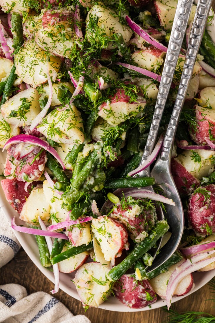 Serving spoon lifting green bean and potato salad with dill and red onion.