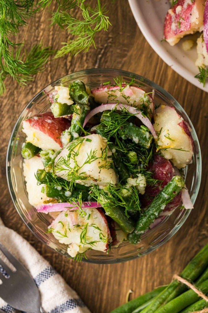 Green bean and potato salad with fresh dill and red onion in a glass bowl.
