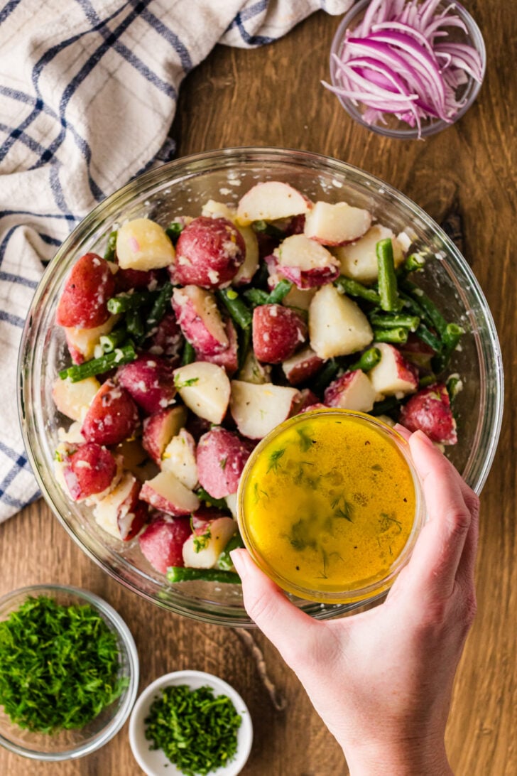 Pouring lemon dill vinaigrette over green bean and potato salad.