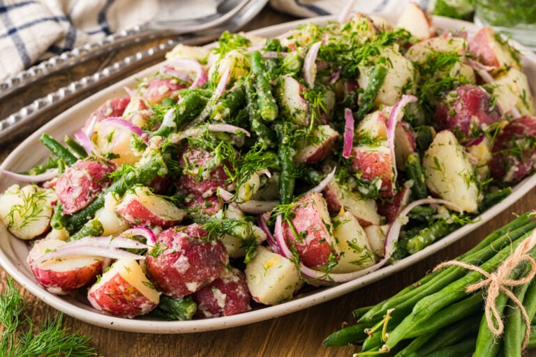 Green bean and potato salad on an oval platter with a bundle of fresh green beans.