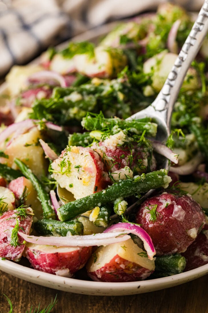Close-up of green bean and potato salad being served with a spoon.