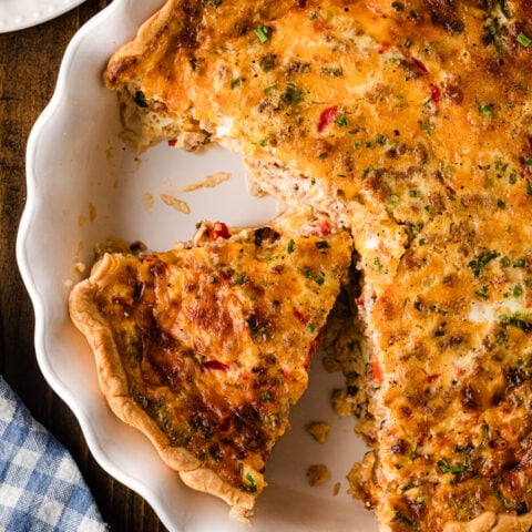 Pimento cheese sausage quiche with a slice served from a golden baked pie crust.