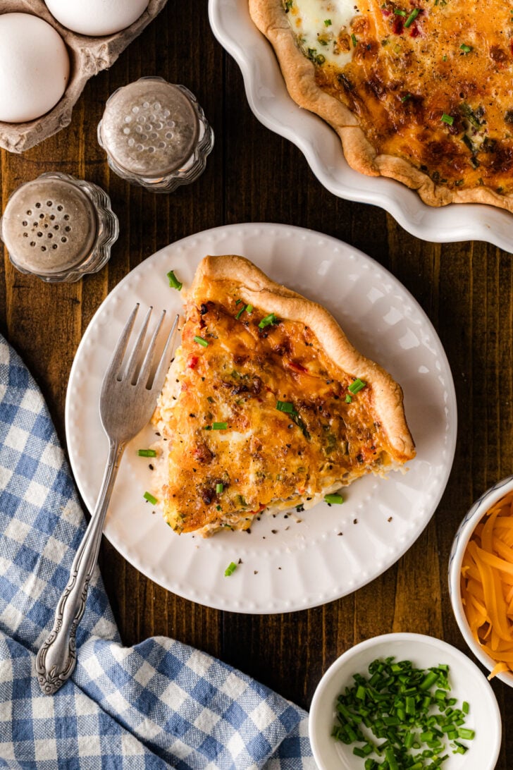 Slice of pimento cheese sausage quiche on a plate with the whole quiche in the background.