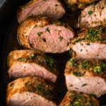 Sliced roasted pork tenderloin in a cast iron skillet with fresh herbs.