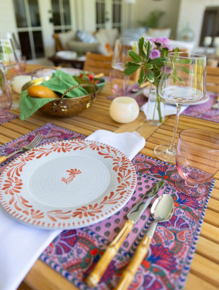 Spring table setting with floral placemats, patterned plate, and gold flatware on a wooden table.