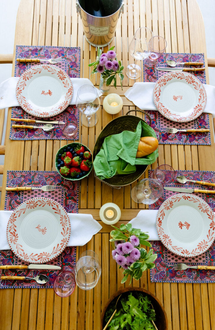 Overhead view of a spring table set for four with floral placemats, wine chiller, and berries.