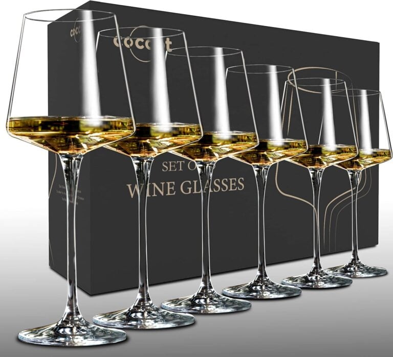 Set of stemmed wine glasses filled with white wine, lined up in front of the packaging box.