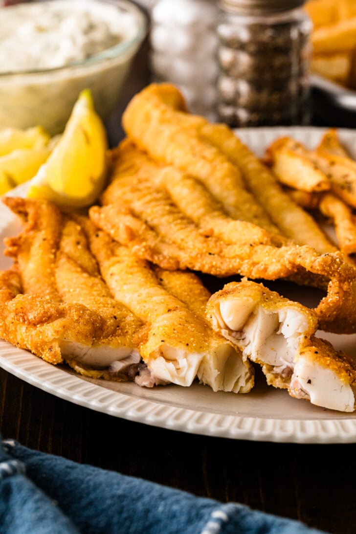 Fried catfish fillets on a platter showing flaky white fish inside the crispy cornmeal crust.