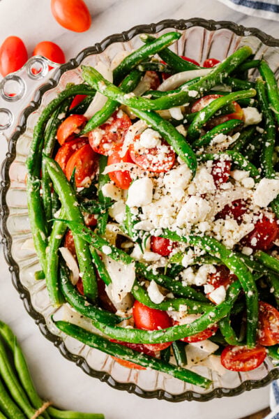 Green bean salad with tomatoes, feta cheese, red onion, and herbs in a glass serving bowl