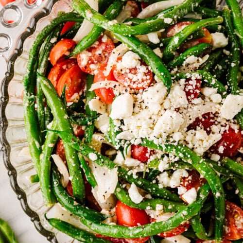 Green bean salad with tomatoes, feta cheese, red onion, and herbs in a glass serving bowl