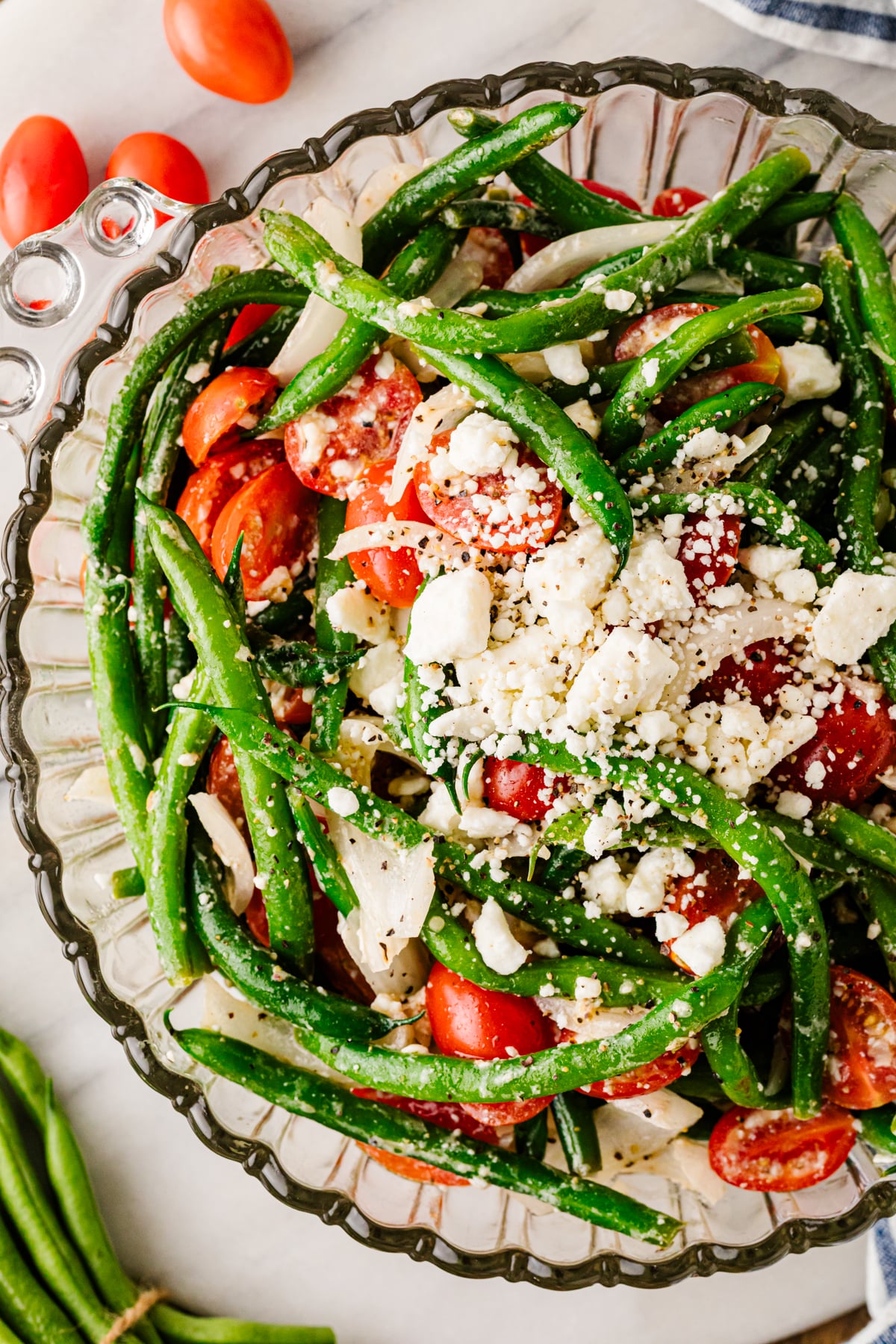 Green bean salad with tomatoes, feta cheese, red onion, and herbs in a glass serving bowl