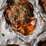 Open foil packs with hamburger patties, carrots, and onions.