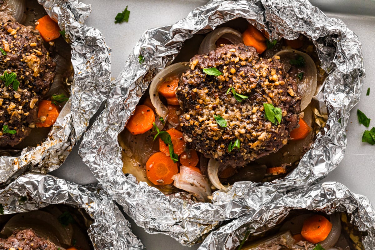 Hobo foil packs with burger patties, carrots, and onions, close-up view.