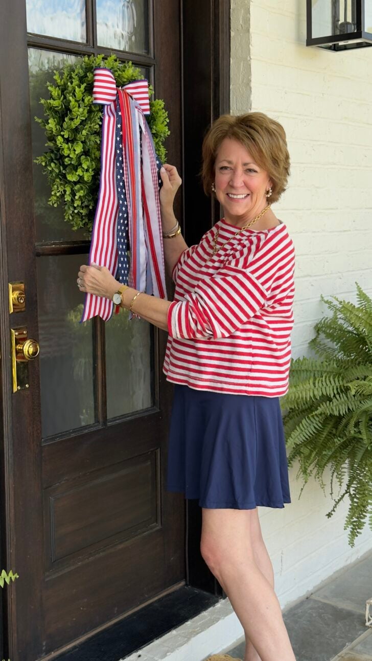 Woman hanging a patriotic ribbon wreath on a front door.