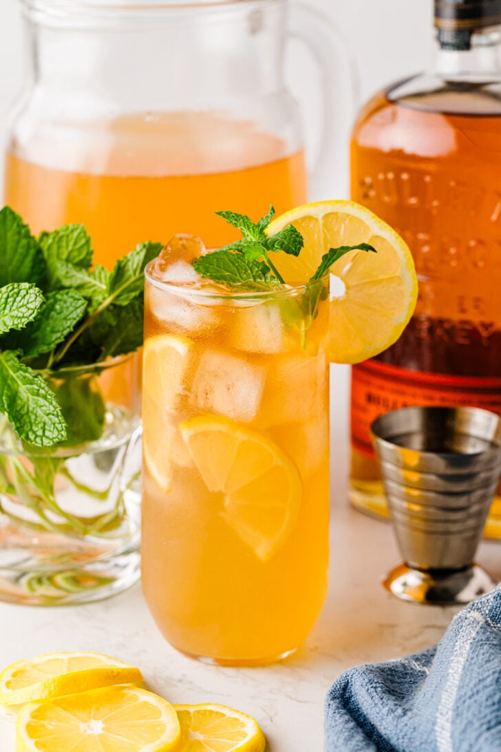 Bourbon Arnold Palmer cocktail with lemon and mint, bourbon bottle in background.