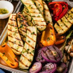 Grilled zucchini, peppers, and onions on a tray with dressing.