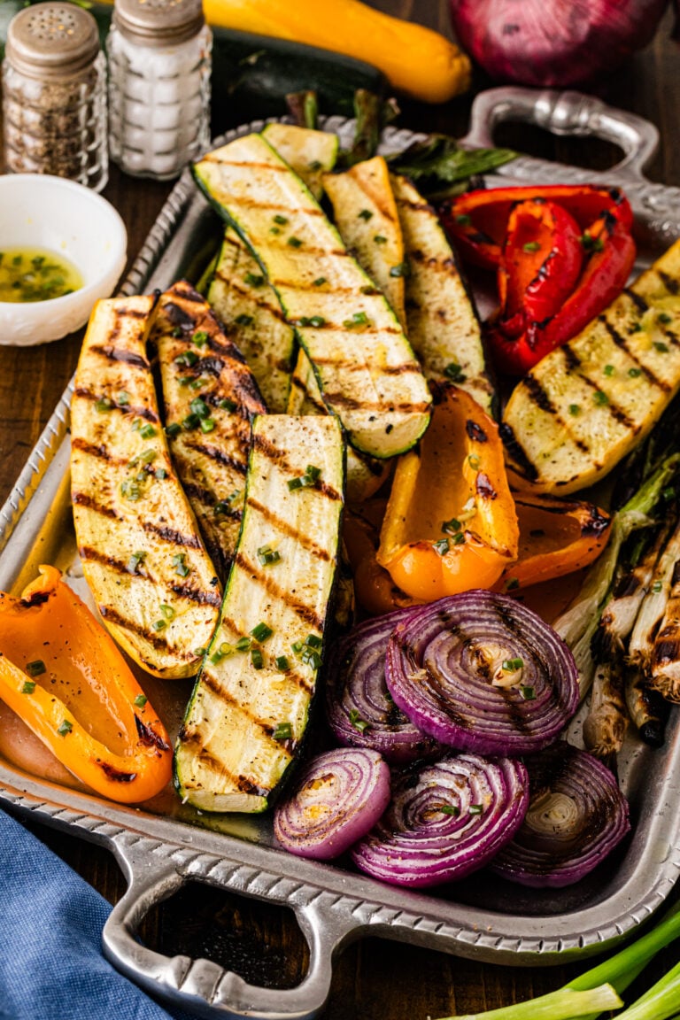 Grilled zucchini, peppers, and onions on a tray with dressing.