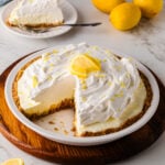 Lemon icebox pie with a slice cut, surrounded by fresh lemons.