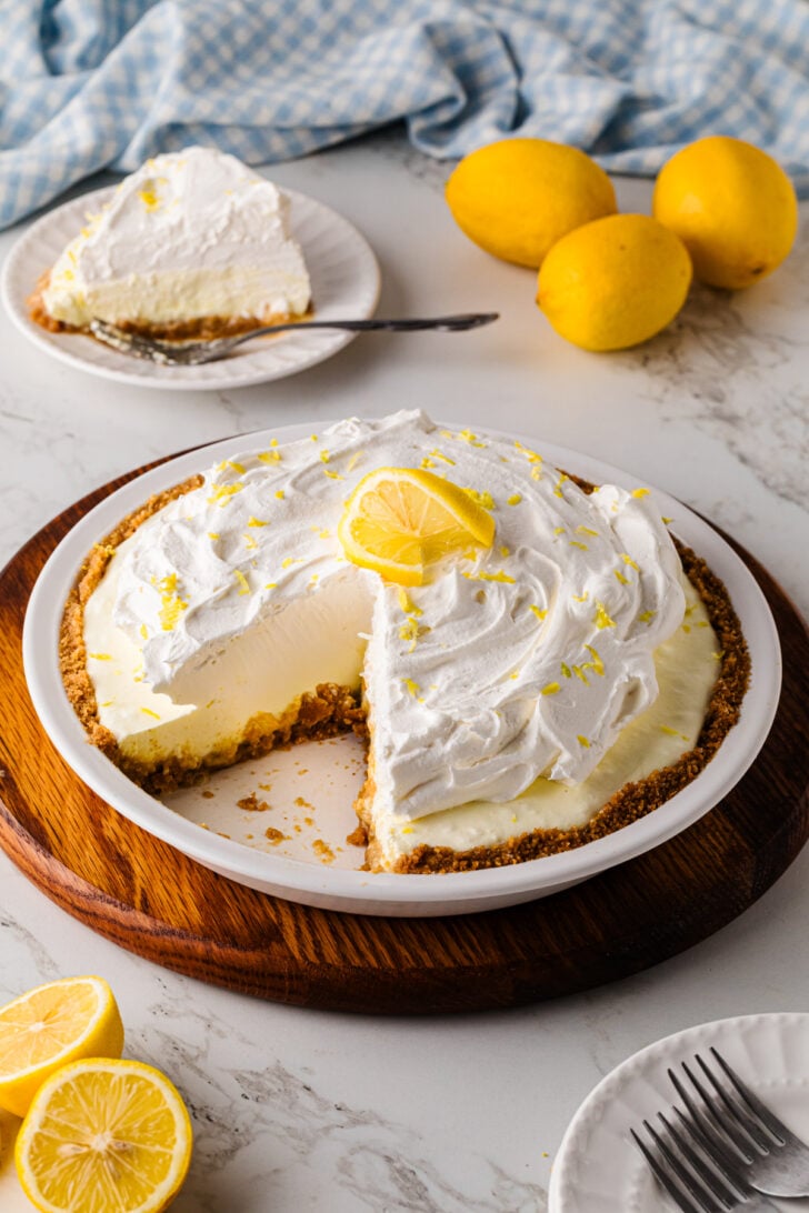 Lemon icebox pie with a slice cut, surrounded by fresh lemons.