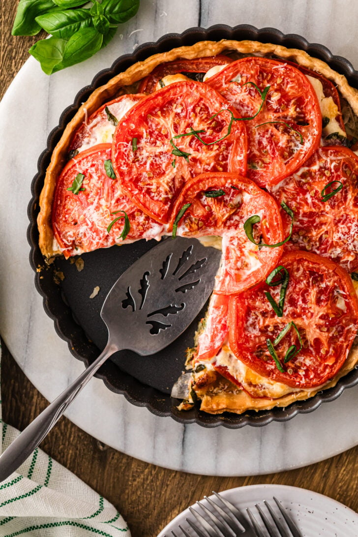 Slice of tomato pie with melted cheese and fresh basil on a plate