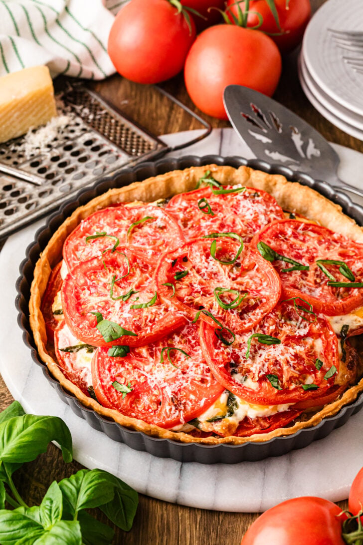 Whole tomato pie in a tart pan with fresh basil and tomatoes.
