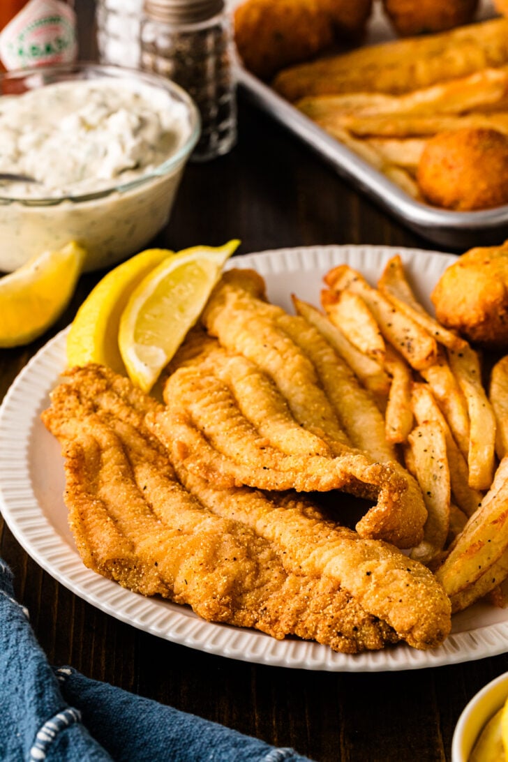Plate of crispy fried catfish fillets with fries, hush puppies, lemon wedges, and tartar sauce