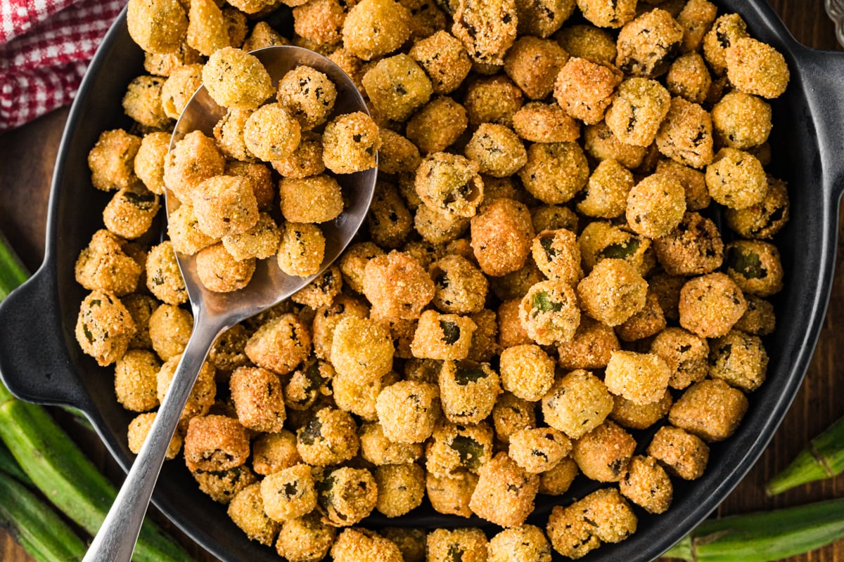 Fried okra in a black skillet with a serving spoon, close-up view.