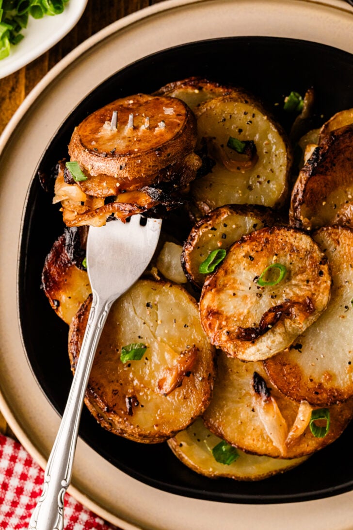 Serving spoon holding fried potatoes and onions from a bowl
