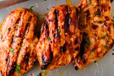 Grilled BBQ chicken breasts with char marks and fresh herbs on a sheet pan.