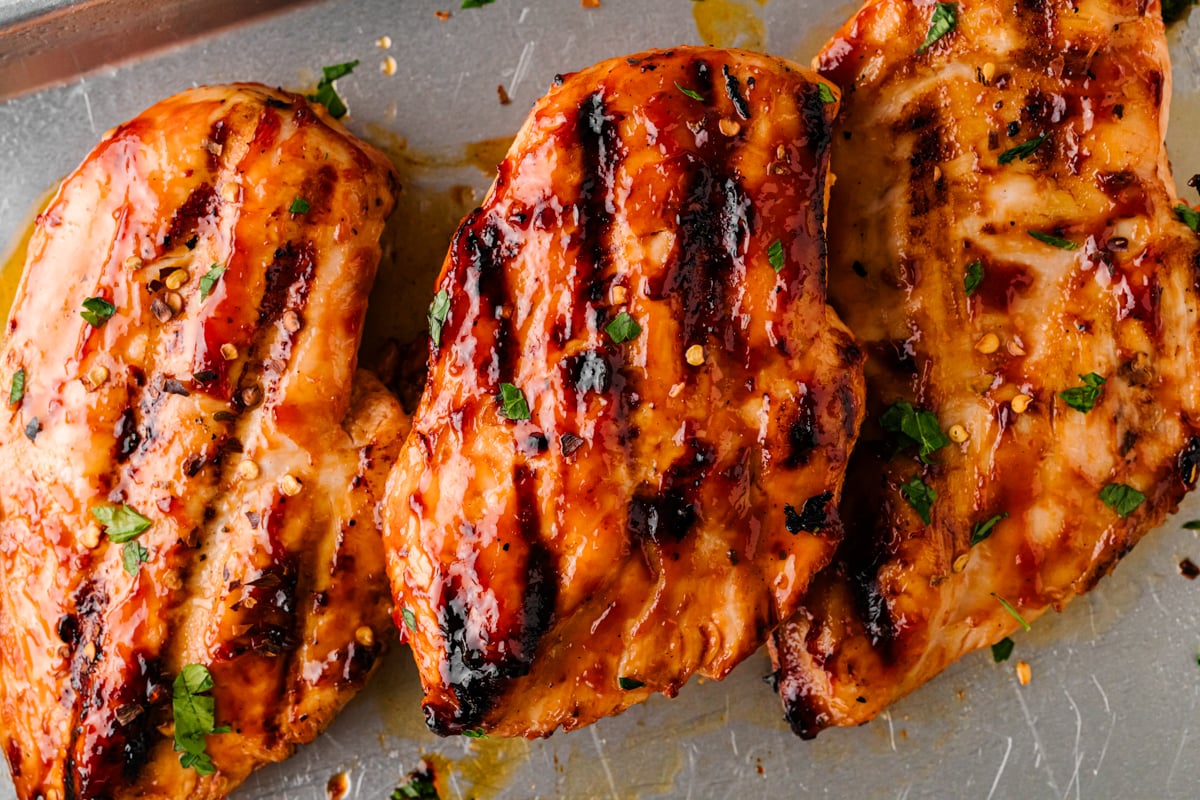 Grilled BBQ chicken breasts with char marks and fresh herbs on a sheet pan.