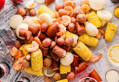 Wide shot of a low country boil spread on newspaper with shrimp, sausage, corn, potatoes, and dipping sauces.